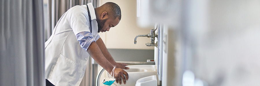 Male doctor leaning against sink and looking down