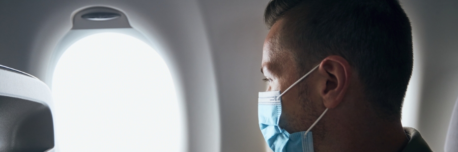 A masked man looking out airplane window