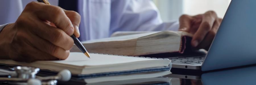 A man at his desk using a laptop, a textbook, and a notebook