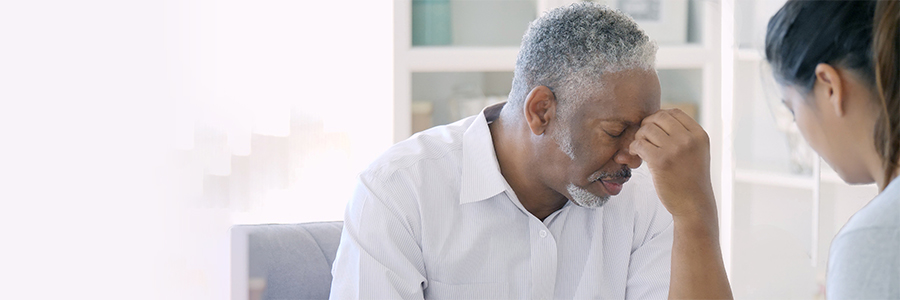 Depressed senior man resting his head with his hands, in discussion with a female mental health professional