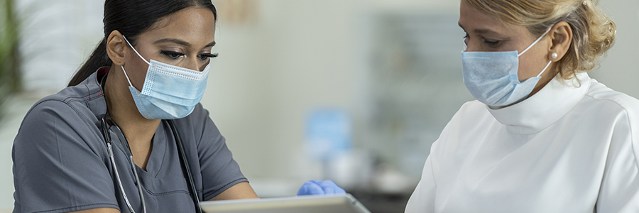 Female patient and female doctor both wearing protective face masks at a medical clinic.