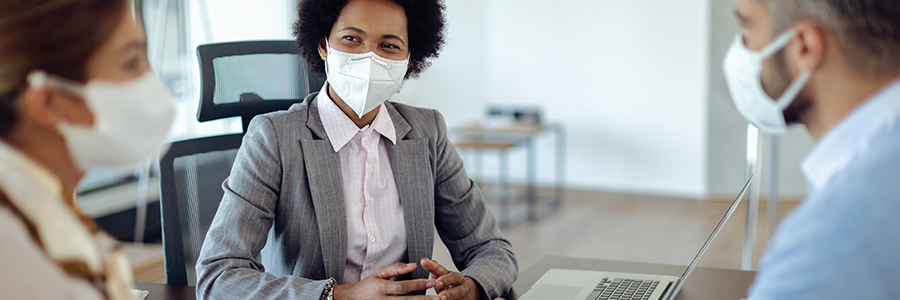 Female hospital administrator meeting with two medical staff, all wearing face masks in an office setting.