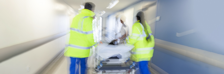 Motion-blurred photograph of a patient on a gurney  being pushed through an emergency room corridor by first responders