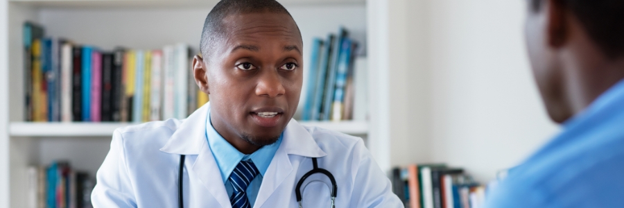 A male physician at his desk speaking with a patient