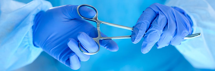 A surgical assistant handing a pair of forceps to a surgeon.