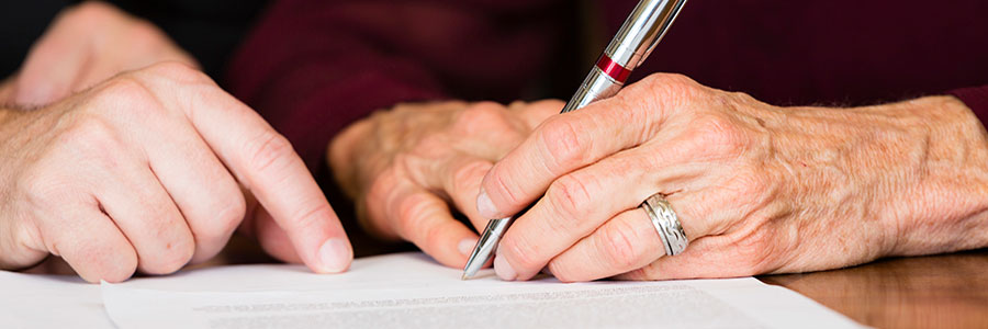 A person signing a document with another person pointing at the text.