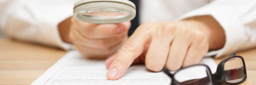 Person holding magnifying glass while reading a paper document.