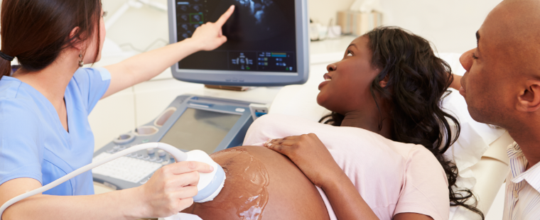 Femme enceinte et son partenaire regardant un moniteur avec une technologue spécialisée en échograph