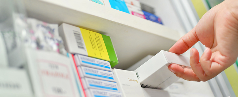 Close-up of a hand reaching for one of many medication boxes on a shelf.