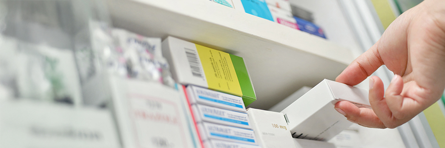 Close-up of a hand reaching for one of many medication boxes on a shelf.