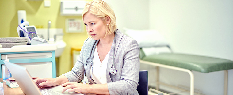 A female physician works at her laptop in her clinical office.