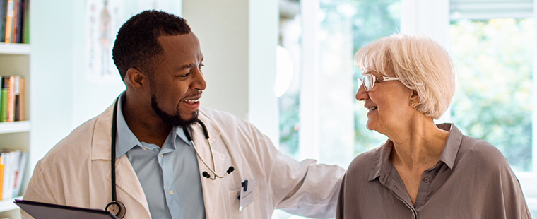 Male physician smiling at elderly female patient as he walks her out of his office.