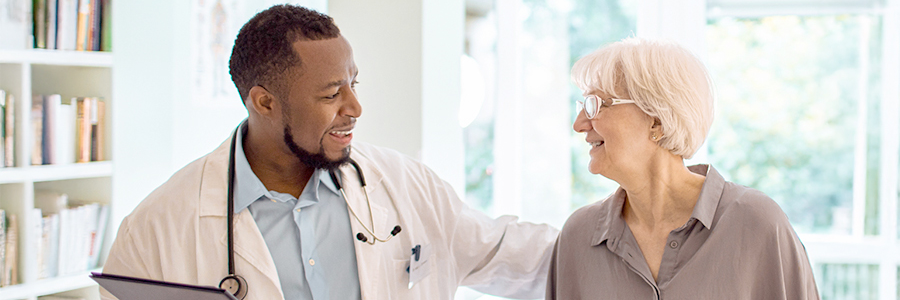 Male physician smiling at elderly female patient as he walks her out of his office.
