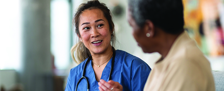 An engaged and smiling female physician is talking to her elderly patient while holding a tablet computer.