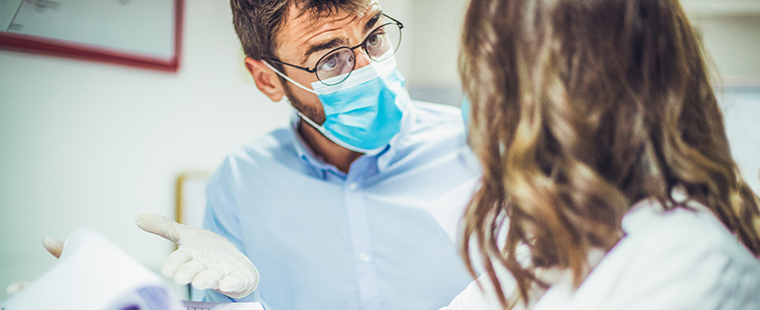 Two physician-colleagues arguing about test results. They are protected with face masks and gloves.