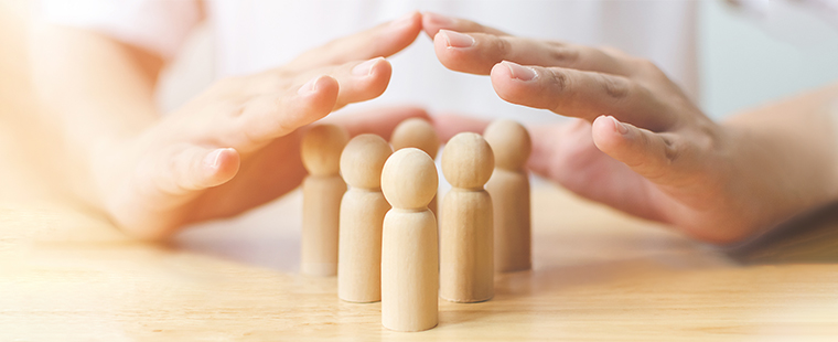 Hands shielding wooden human figures on a table.