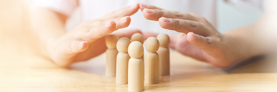 Mains protégeant des figurines humaines en bois sur une table.