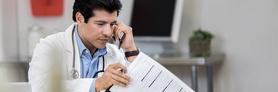 Male physician talks with colleague on the phone while reviewing a patient’s chart.