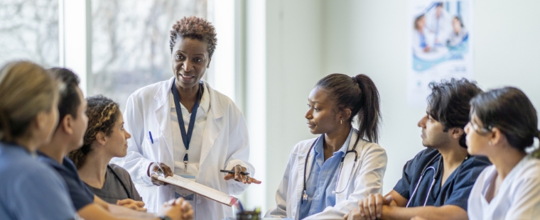 Une médecin écrit tout en expliquant une intervention à des apprenants regroupés autour d’elle.