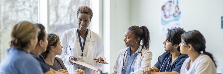 A female physician writes as she explains procedures to trainees around her.