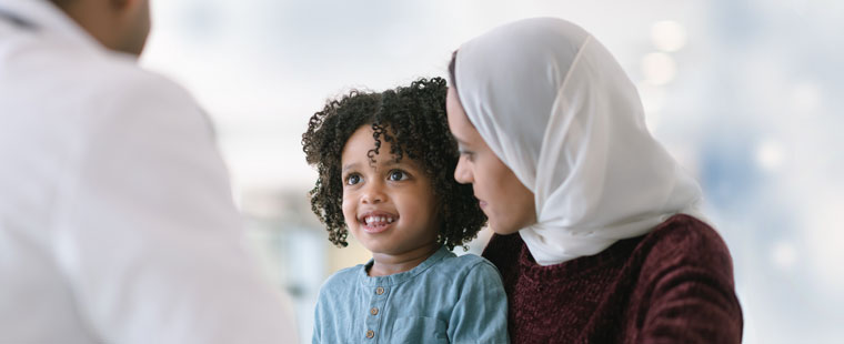 Un jeune enfant qui sourit au médecin, assis sur les genoux d’une femme portant le foulard.