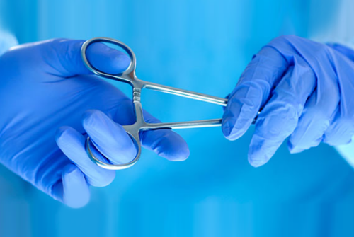 A surgical assistant handing a pair of forceps to a surgeon.