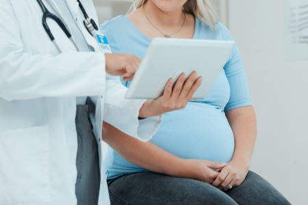 A physician shares information from a tablet with a pregnant patient