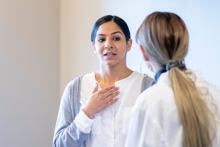 A female patient gestures to her own chest while talking with her doctor.
