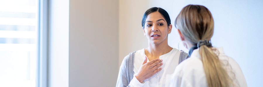 A female patient gestures to her own chest while talking with her doctor.