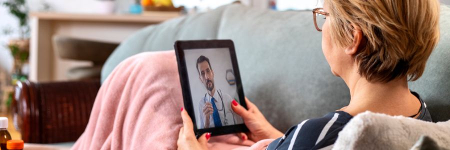 Femme qui est assise sur un sofa et qui participe à un appel vidéo avec un médecin au moyen d’une tablette.