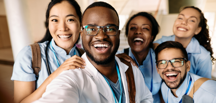 Cinq médecins en résidence de différentes origines ethniques sourient à la caméra en prenant un égop