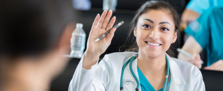 Young female physician raising hand smiling.